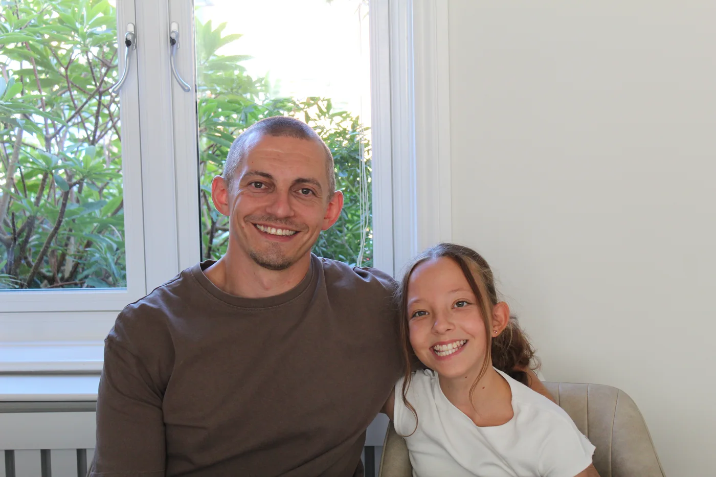 Jamie Foster and his daughter Isla sitting together by a window, smiling